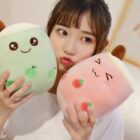 Two bubble tea plushies, a green melon and pink strawberry design, displayed with a person.