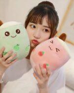 Two bubble tea plushies, a green melon and pink strawberry design, displayed with a person.