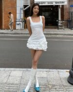 A woman wearing a white ruffled summer dress, embodying the coquette aesthetic, outdoors.