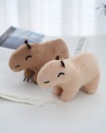 Two brown capybara plush keychains on a table next to a magazine.