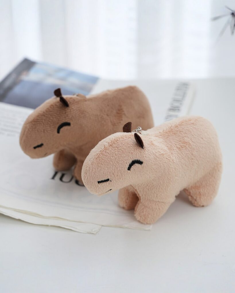 Two brown capybara plush keychains on a table next to a magazine.
