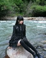 Woman wearing a black laced gothic lolita dress by a river.