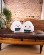 Kawaii onigiri plushies displayed on a leather ottoman. Cute, smiling characters with rice ball details.