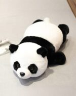 A cute kawaii panda plushie lying on a gray surface. It’s a soft, black and white stuffed animal.