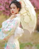 A woman wearing a japanese floral kimono with pink and blue flowers, holding a lace parasol.