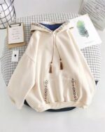 Close-up of a light beige ethno-chic hoodie with embroidered details and tassels.
