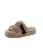 Light brown fluffy hand holding slippers with a black bow detail.