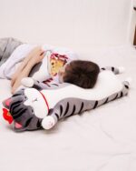 Long cat plushie, Whiskers the Stripped Emperor Cat, resting on a bed.