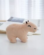 Tan capybara plush keychain on a white table with a book.