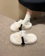 Pair of fluffy hand holding slippers in beige, featuring cute sheep-shaped details.
