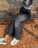 Long y2k denim skirt worn by a person on a park bench, featuring a relaxed fit.
