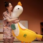 Large white banana duck plushie with yellow tail and orange beak, hugging a person.