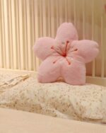Pink sakura flower pillow resting on a floral bedspread. A sakura flower pillow.