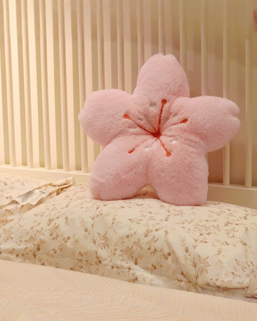 Pink sakura flower pillow resting on a floral bedspread. A sakura flower pillow.