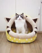 A yellow and white kawaii cat bed with cat ears, featuring a gray cat inside.