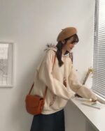 Woman wearing an ethno-chic hoodie with embroidery, beret, and crossbody bag.