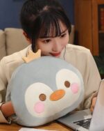 Round animal hand warmer plushie featuring a gray penguin, resting on a desk.