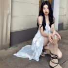 Woman wearing a white ruffled sling dress - Coquette aesthetic dress, casual street style with boots and iced coffee.
