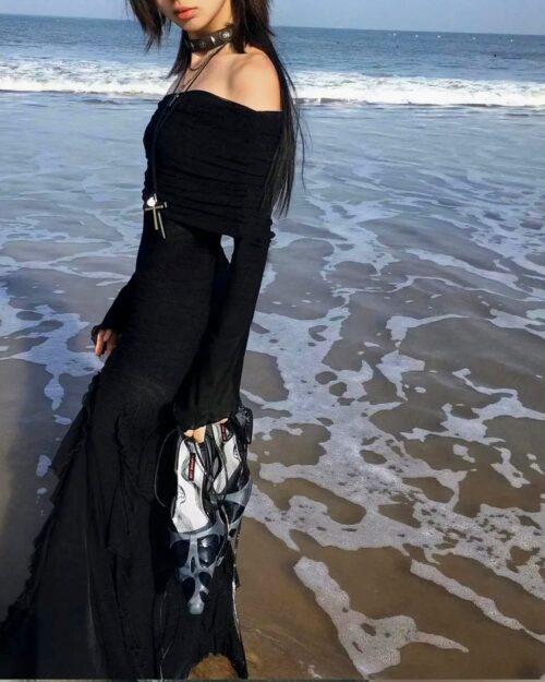 Black gothic aesthetic dress on a beach, featuring a dramatic, flowing silhouette and long sleeves.
