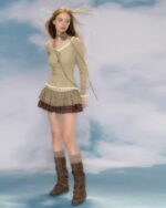 Model wearing a beige vintage aesthetic cardigan, plaid skirt, and boots.