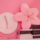 Pink sakura flower pillow resting on a stack of books with a clock.