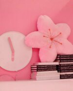 Pink sakura flower pillow resting on a stack of books with a clock.