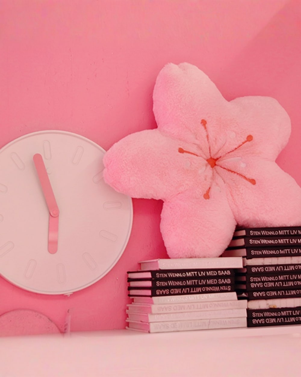 Pink sakura flower pillow resting on a stack of books with a clock.