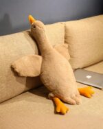 A large, plush goose toy (big goose plush) resting on a sofa with a laptop.