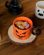 Orange halloween pumpkin cup with a black handle and jack-o'-lantern design, holding candy.
