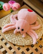 Close-up of a pink spooky cute spider plush toy with long legs and small eyes.
