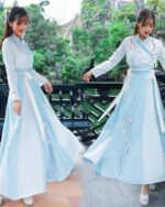Woman wearing a light blue hanfu summer dress with floral embroidery, outdoor setting.