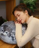 A woman resting her head on a Yuki the seal plush, depicting a gray seal with a white pattern.