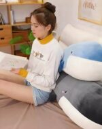 Blue kawaii whale plushie resting on a bed with a person reading.