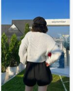 White thick knit vintage aesthetic cardigan worn with black shorts and beret.