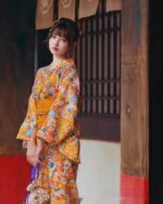 Woman wearing a flower summer yukata featuring a floral pattern in shades of yellow and orange.