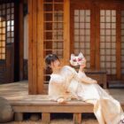 A woman wearing a Hanabi Pattern Summer Yukata - Japanese Aesthetic, holding a fox mask, posing outdoors.