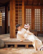 A woman wearing a Hanabi Pattern Summer Yukata - Japanese Aesthetic, holding a fox mask, posing outdoors.