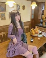 Woman wearing a purple lace gothic aesthetic dress, seated at a wooden table in a vintage interior.