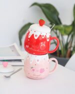 Two strawberry ceramic mugs stacked together, featuring pink and red designs with strawberry details.