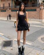 Woman wearing a ruffled summer dress, coquette aesthetic dress, with a black tank top and boots.