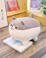Grey super fat shiba plushie lies on a stack of books.