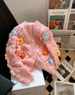 Pink handmade aesthetic cardigan with floral embellishments and cable knit design.