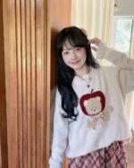 Woman wearing a cottagecore bear sweater with an apple design and plaid pants.