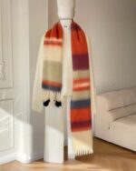 Fluffy rainbow scarf displayed on a mannequin, featuring colorful striped design and pom-poms.
