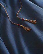Close-up of a blue ethno-chic hoodie featuring drawstring tassels with wooden and red beads.