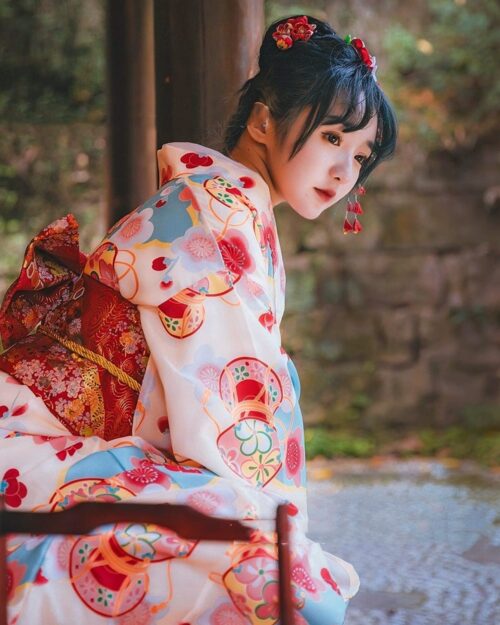 Pink new year kimono featuring floral and traditional Japanese design; woman wearing festive attire outdoors.