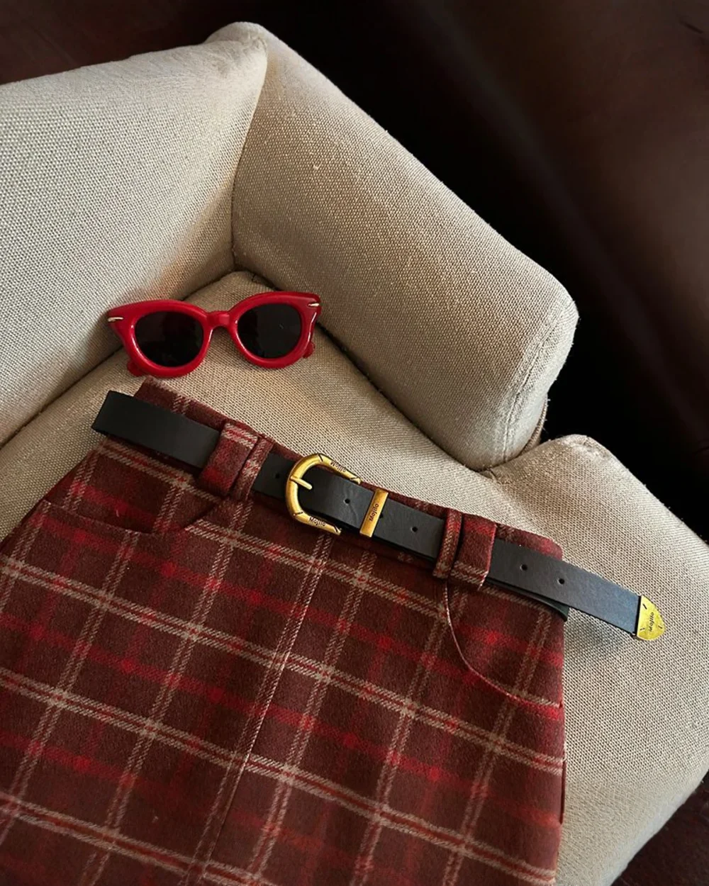 Plaid mini skirt featuring a preppy aesthetic, styled with sunglasses and a belt.