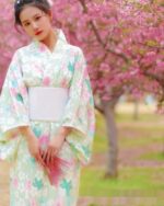 Woman wearing a japanese floral kimono outdoors amidst cherry blossoms.