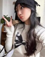 Woman wearing a white korean aesthetic sweater with a bowknot print design.
