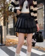 Black pleated korean aesthetic skirt worn by a person, detailed with a layered top and accessories.